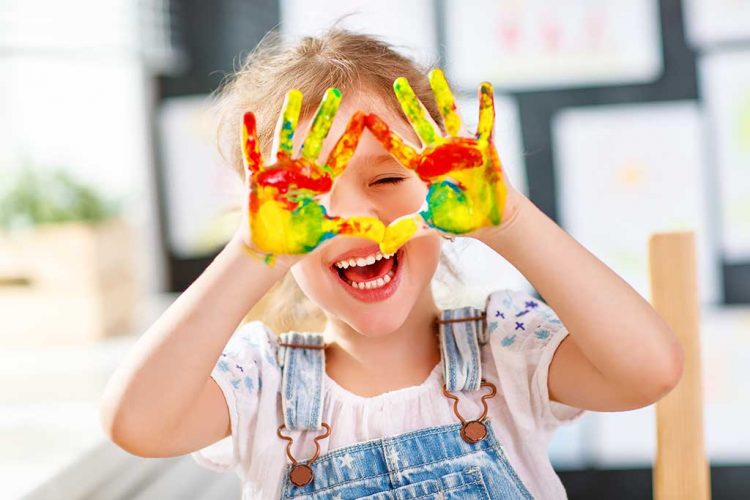 funny child girl draws laughing shows hands dirty with paint